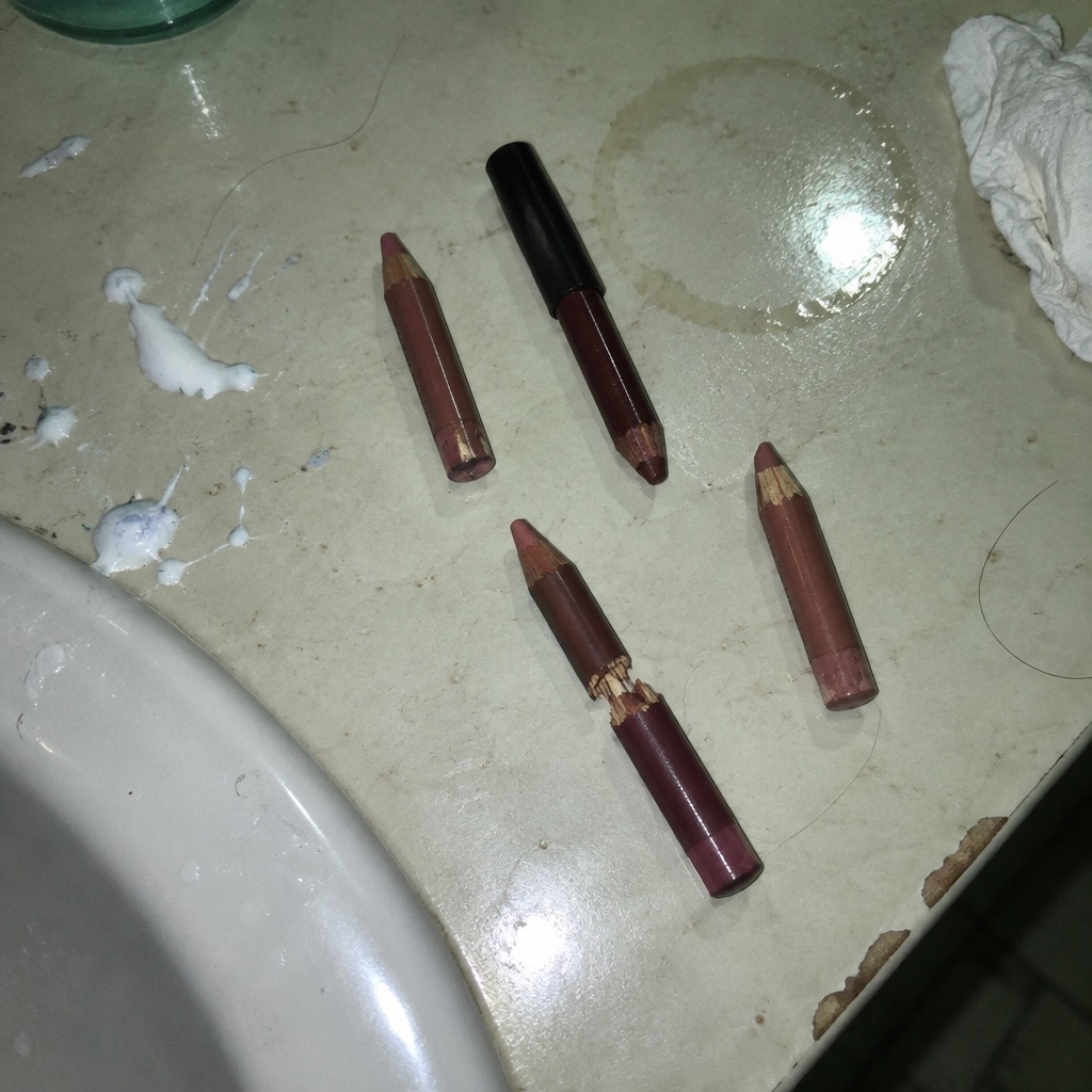Four worn lip liner pencils on a bathroom counter